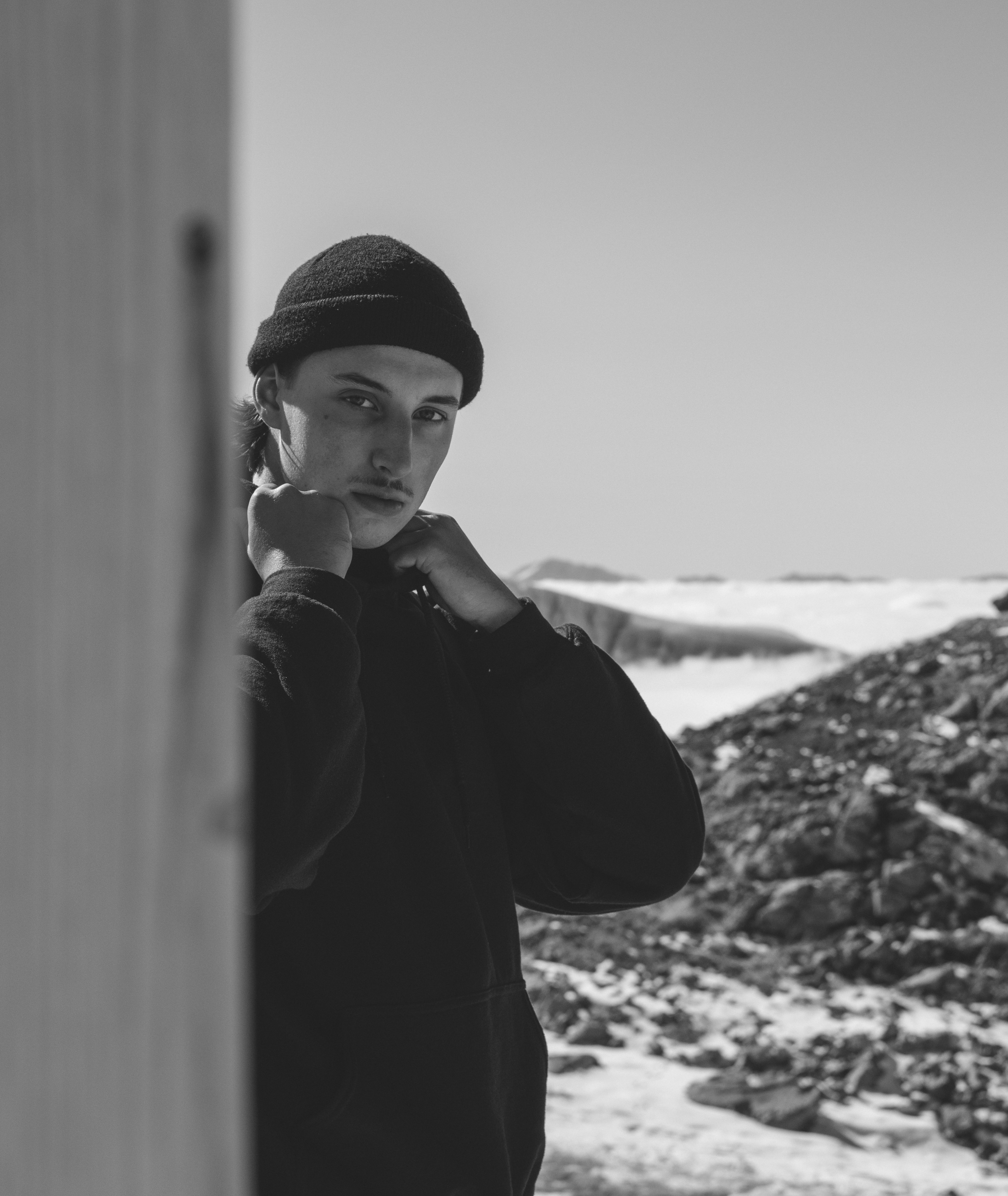 grayscale photo of woman in black jacket and knit cap leaning on wall